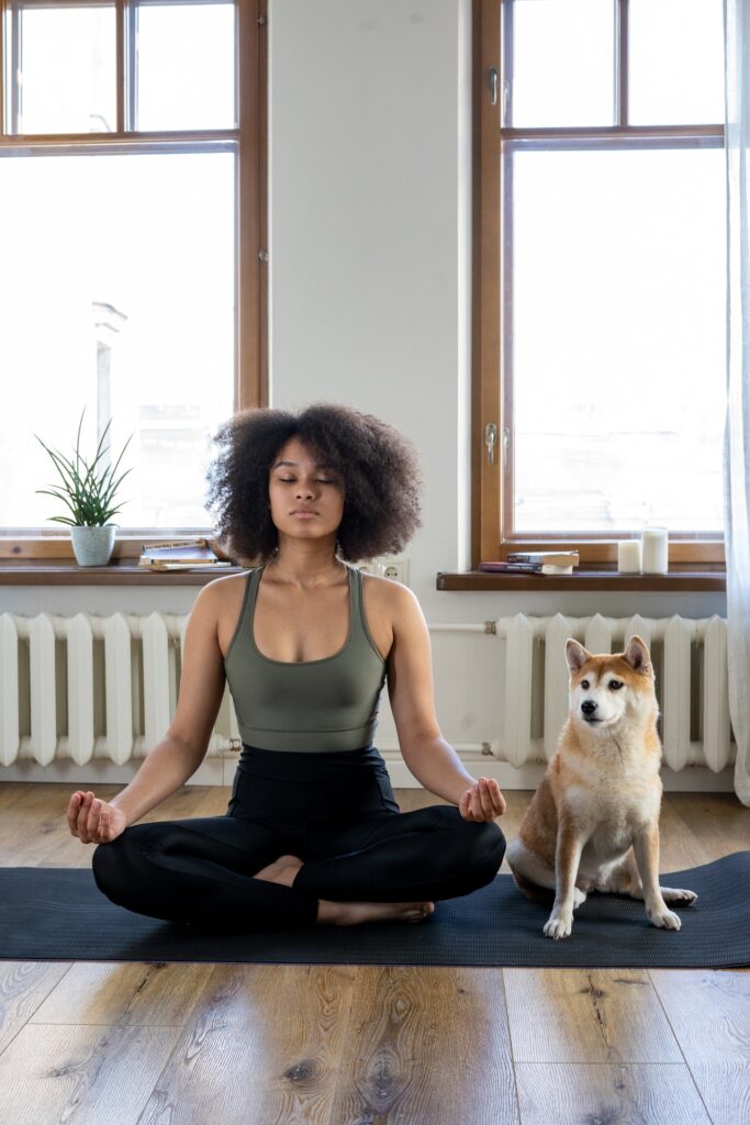 Woman meditating on a yoga mat with her dog