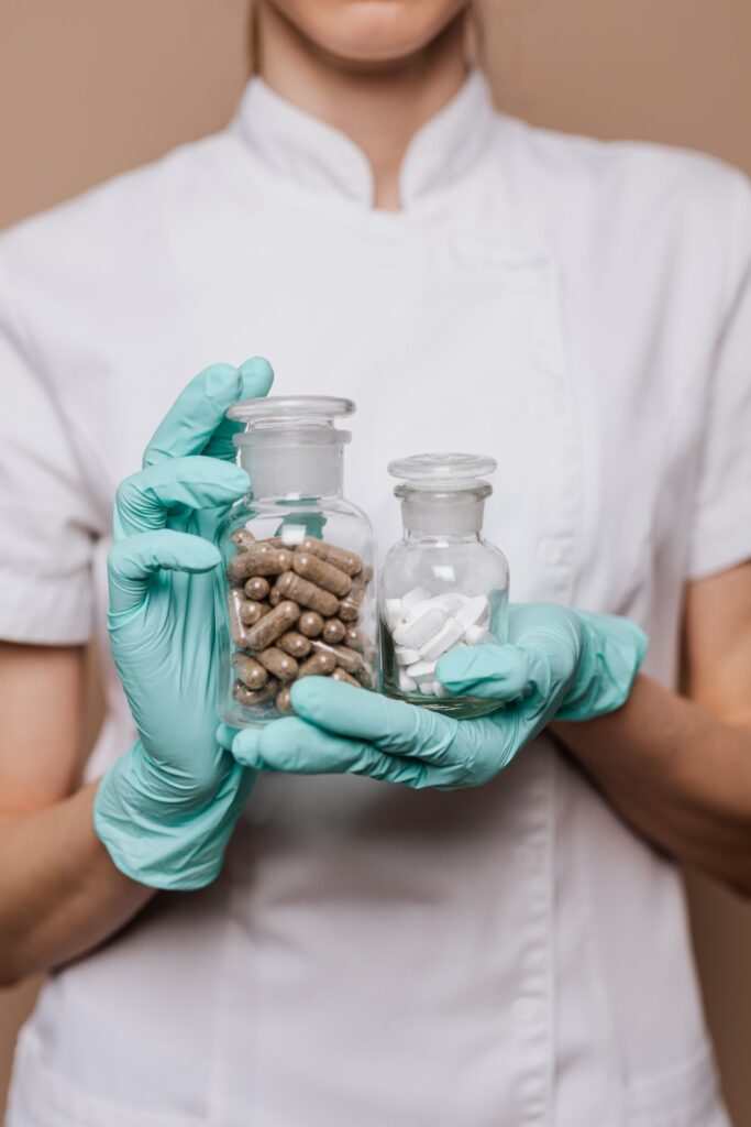A medical professional holding a bottle of brown pills and a bottle of white pills