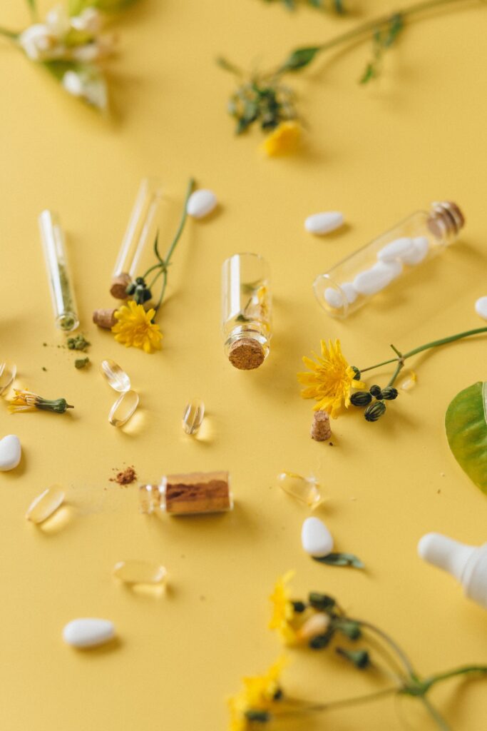Pills, small glass bottles and florals laying on a yellow table
