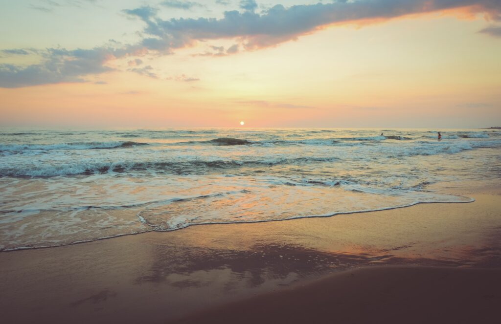 waves coming onto a sandy seashore at sunset