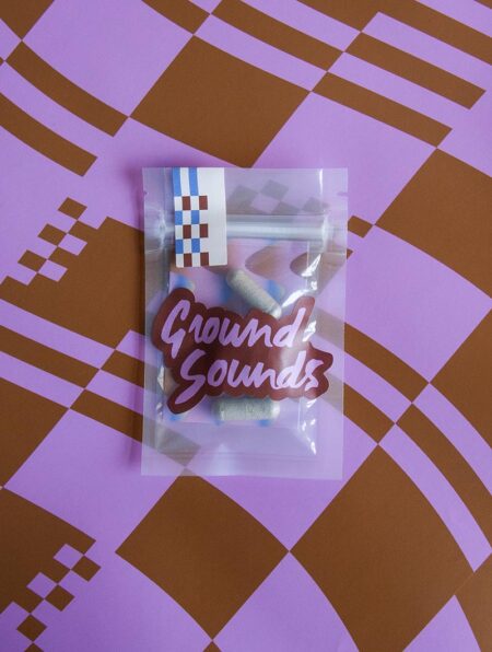 A plastic bag with four Higher Ground pills inside on a purple and brown checked background