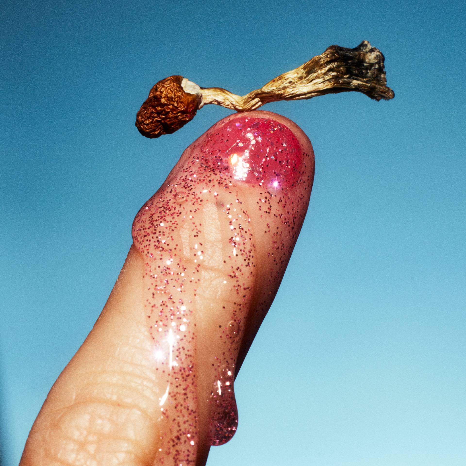 A finger covered in glitter goop with a mushroom perched ontop